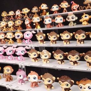 Può includere: Una collezione di piccole figurine di scimmia colorate esposte su scaffali a più livelli. Le scimmie variano di colore, tra cui marrone, rosa e beige, con tratti del viso dettagliati e grandi occhi. L'esposizione è ben illuminata.