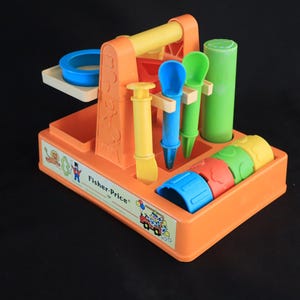 Puede incluir: Un juego de herramientas de juguete Fisher-Price naranja con varias herramientas coloridas. Incluye un anillo azul, herramientas amarillas y azules, un cilindro verde y bloques coloridos. El juego tiene un asa y una bandeja.
