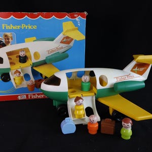 Op de afbeelding: Een vintage Fisher-Price speelgoedvliegtuig met een wit, groen en geel kleurenschema. Het speelgoed heeft een open zijkant en bevat verschillende kleine plastic figuren en bagage. De doos is zichtbaar op de achtergrond.