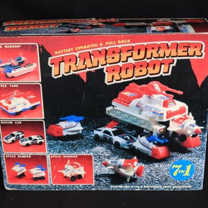 Könnte beinhalten: Vintage "Transformer Robot" Spielzeugbox mit einem roten, weißen und blauen Roboter und verschiedenen Fahrzeugen. Die Box zeigt ein 7-in-1-Spielzeug mit Bildern eines Raumschiffs, eines Panzers, eines Rennwagens und mehr. Der Text "Battery Operated & Pull Back" ist sichtbar.