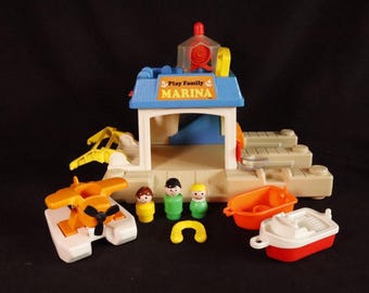 Puede incluir: Un juego de juguetes vintage Fisher-Price Play Family Marina. El juego incluye un edificio de puerto deportivo con techo azul, una grúa amarilla, un hidroavión, un bote y tres figuras. El edificio del puerto deportivo tiene la palabra "Marina" en el frente.