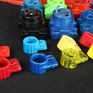 May include: A collection of colorful plastic toy parts in various colors, including red, blue, green, yellow, and black. The parts include cylindrical rings and larger, blocky components with pegs and slots, suggesting a construction or assembly toy.