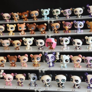 Puede incluir: Una colección de pequeñas figuras de animales coloridos, incluyendo pandas y osos, dispuestas en estantes escalonados. Las figuras son de varios colores, incluyendo marrón, blanco, morado y amarillo. La colección está sobre un fondo negro.