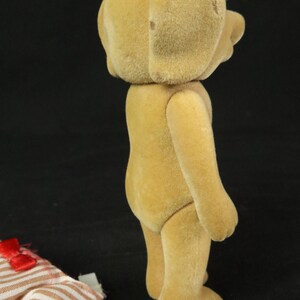 May include: A tan, flocked, anthropomorphic dog figurine standing in profile. The figure has a smooth, fuzzy texture and is wearing black plastic glasses. Beside the figurine lies a piece of fabric with a brown and white striped pattern.
