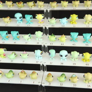 May include: A display of small animal figurines in various colours, arranged on a multi-tiered white shelf. The figurines are in different poses, including green, yellow, blue, and purple. Each shelf is labelled with numbers.