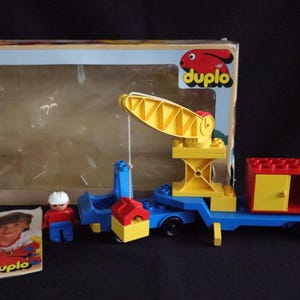 Op de afbeelding: Een Duplo constructieset met een gele kraan, blauwe vrachtwagen, rode en gele bouwstenen en een kleine figuur. De set zit in de originele doos, met het Duplo logo zichtbaar.
