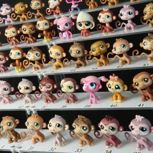 Puede incluir: Colección de pequeñas figuras de monos coloridos exhibidas en estantes escalonados. Los monos varían en color, incluyendo marrón, rosa y amarillo, con ojos grandes y colas rizadas. Las figuras están numeradas.
