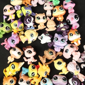 May include: A collection of colorful, small plastic animal figurines. The toys feature various animals, including cats, dogs, birds, and monkeys, in a variety of colors such as pink, yellow, orange, and purple. Each figurine has large, expressive eyes.