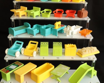 Puede incluir: Una colección de coloridos muebles y accesorios de juguete de plástico en miniatura, que incluyen sillas, camas, mesas, una bañera y un tobogán. Los juguetes están dispuestos en estantes de exhibición transparentes sobre un fondo negro.