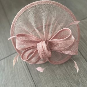 May include: A blush pink fascinator with a large bow and feathers.
