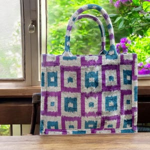 Może przedstawiać: Torba typu tote w kolorze fioletowym i turkusowym z geometrycznym wzorem. Torba ma dwa uchwyty i jest wykonana z miękkiej, fakturowanej tkaniny.
