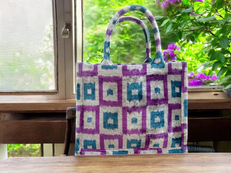 Może przedstawiać: Torba typu tote w kolorze fioletowym i turkusowym z geometrycznym wzorem. Torba ma dwa uchwyty i jest wykonana z miękkiej, fakturowanej tkaniny.