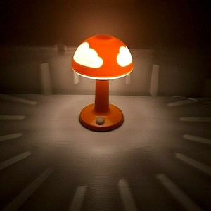 May include: Orange mushroom-shaped table lamp with white cloud cutouts in the shade. The lamp is on and casting a shadow on the surface it is sitting on.
