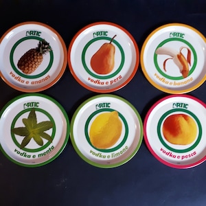 May include: Six round, white, ceramic coasters with green, orange, yellow, and red borders. Each coaster features a different fruit or leaf design and the text "ARTIC vodka e [fruit name]" in black.