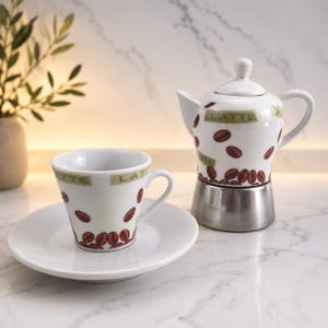 May include: A white ceramic espresso cup and saucer set with a matching coffee maker. The cup, saucer, and coffee maker are decorated with brown coffee bean graphics and the word "LATTE". The coffee maker has a silver base.