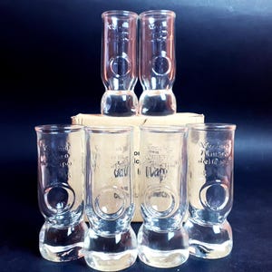 Può includere: Set di sei bicchieri da shot in vetro trasparente con base rotonda. I bicchieri hanno un cerchio rialzato al centro e sono incisi con il testo "Marciano 7 Marzo del 1950".