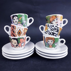 Op de afbeelding: Een set van zes witte keramische espressokopjes en schoteltjes, gerangschikt in twee stapels. Elk kopje is voorzien van een unieke kleurrijke illustratie, waaronder portretten en decoratieve patronen in groen, oranje, zwart en roze.