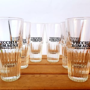 Könnte beinhalten: Sechs klare, geriffelte Trinkgläser mit dem Text "VECCHIA ROMAGNA etichetta nera" in Schwarz aufgedruckt. Die Gläser sind auf einer Holzoberfläche angeordnet.