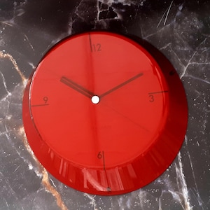 Könnte beinhalten: Eine runde, rote Wanduhr mit schwarzen Zeigern und einem weißen Mittelpunkt. Das Zifferblatt hat schwarze Ziffern an den Positionen 12, 3, 6 und 9 Uhr. Die Uhr ist ein modernes Design.