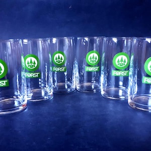 May include: Set of six clear drinking glasses. Each glass features a green and white logo with the word "FORST" in a green rectangle. The glasses are cylindrical and appear to be made of glass.
