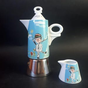 May include: A vintage espresso maker with a whimsical design. The blue ceramic body features a cartoon figure and floral accents. A matching creamer is also present. The base is stainless steel, and the handle and lid are white.