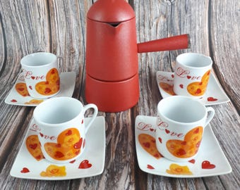 May include: A red stovetop espresso maker with a matching handle and a silver knob, accompanied by four white espresso cups and saucers. The cups and saucers feature a heart design with the word "Love".