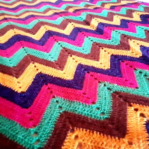 Könnte beinhalten: Eine bunte gehäkelte Decke mit einem Zickzackmuster in den Farben Pink, Grün, Braun, Gelb und Blau.