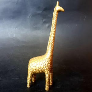 May include: A gold-coloured giraffe figurine with a textured, patterned surface. The giraffe has a long neck and stands on four legs. The figurine is a decorative item, likely for a shelf or desk.