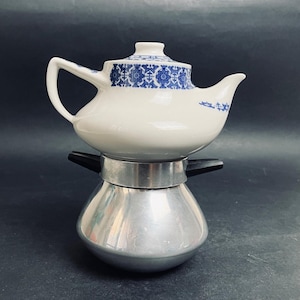 May include: A white teapot with a blue floral design on the lid and a silver base. The teapot has a curved handle and spout. The base is a silver coffee maker. The teapot is a vintage style.