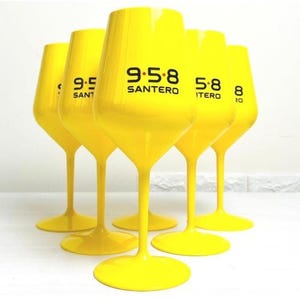 Könnte beinhalten: Sechs gelbe Weingläser mit schwarzem Text. Der Text auf den Gläsern lautet "9.5.8 SANTERO", "9.5 SANTERO", "5.8 ITEO", "5.8 ITEO" und "8 ITEO".