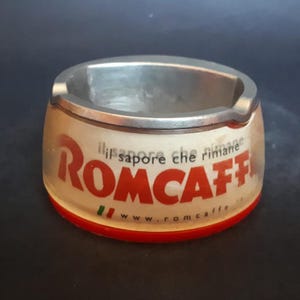 Peut inclure: Un cendrier rouge et blanc avec les mots "Il sapore che rimane" et "ROMCAFFÈ" et le site web "www.romcaffe.it" imprimés dessus.
