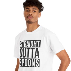 Puede incluir: Camiseta blanca con el texto "STRAIGHT OUTTA SPOONS" en negro y negrita. La camiseta es de estilo cuello redondo. El modelo lleva vaqueros azules.