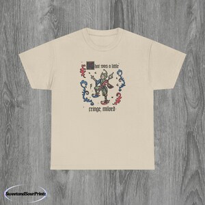 May include: Beige t-shirt with a medieval-style illustration of a jester playing a stringed instrument. The text "that was a little" and "cringe, milord" are printed above and below the jester graphic.