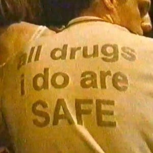 以下が含まれることがあります： 「all drugs i do are SAFE」と印刷された黄色のシャツを着ている人