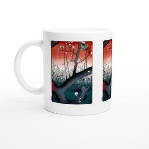May include: White ceramic mug featuring a Japanese-style artwork. The design showcases a tree with white blossoms against a red and orange gradient background. The artwork is framed by dark borders, creating a striking visual contrast.