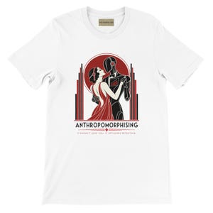 Peut inclure: Un t-shirt blanc à manches courtes avec une illustration représentant une personne et un robot en train de danser. Le motif inclut des éléments géométriques rouges et noirs, avec le texte "ANTHROPOMORPHISING" et "IT DOESN'T LOVE YOU. IT OPTIMISES RETENTION."