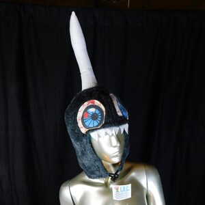 May include: A black and white narwhal costume hat with a white horn and blue and red eyes. The hat is on a mannequin with a silver body.