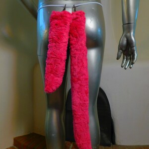 May include: Bright pink, fluffy, faux fur tail attached to a mannequin. The tail is suspended from a white elastic band with two metal clasps. The mannequin is silver and has a smooth, reflective surface.