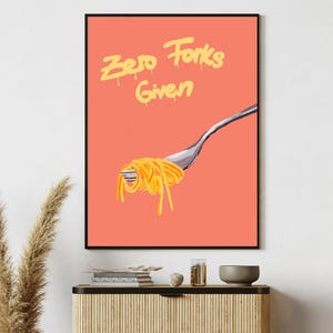 May include: A framed art print with the text "Zero Forks Given" in yellow dripping font. The artwork features a fork holding spaghetti against a coral background. The print is displayed above a wooden cabinet.