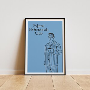 Könnte beinhalten: Gerahmter Kunstdruck mit blauem Hintergrund und dem Text "Pyjama Professionals Club". Die Illustration zeigt eine Person in gestreiftem Pyjama, die eine Tasse hält und eine Schlafmaske trägt. Das Kunstwerk wird auf einem Holzboden ausgestellt.