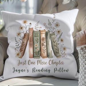 May include: White reading pillow with a floral design and the text "Just One More Chapter Jayne's Reading Pillow." The pillow features a watercolor illustration of books and daisies. The books are in shades of brown, green, and peach.