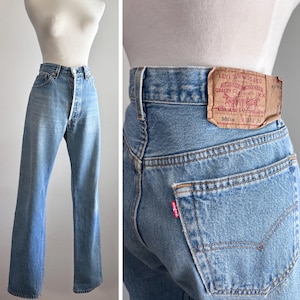 May include: Light blue denim jeans with a high-waisted fit and straight legs. The back features a tan leather patch with the text Levi Strauss & Co. Quality Clothing XX 501xx 34 34 and a small red tab on the back pocket with the word Levi's.