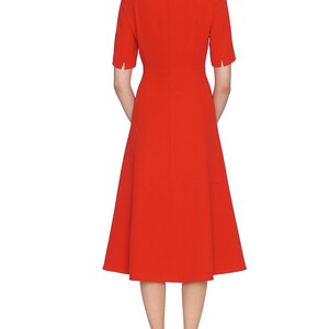 May include: A vibrant red midi dress featuring a round neckline, short sleeves with small side slits, and a fitted bodice that transitions into a flared skirt. The garment includes a vertical seam down the center back and a concealed zipper closure.