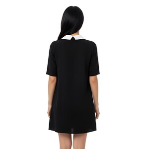 Puede incluir: Un vestido negro con cuello blanco y mangas cortas. El vestido es de dise&ntilde;o sencillo y cl&aacute;sico, adecuado para diversas ocasiones. La modelo est&aacute; de espaldas a la c&aacute;mara.