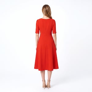 May include: A vibrant red midi dress featuring short sleeves with small slits at the cuffs, a round neckline, and a fitted bodice that transitions into a flared skirt. The back of the dress includes a vertical seam and a concealed zipper closure.
