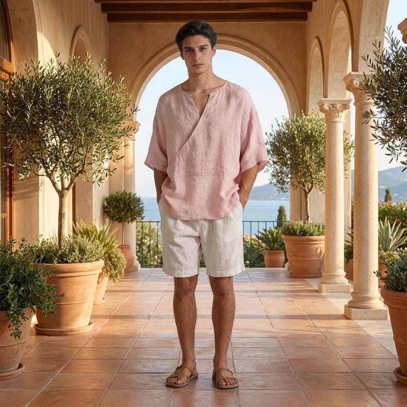 May include: A person wearing a light pink linen wrap top and white linen shorts. The outfit is paired with brown sandals. The person is standing on a tiled patio with potted plants and a view of the ocean.