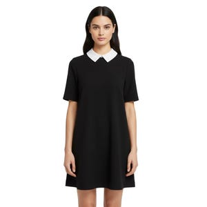 Puede incluir: Un vestido negro con cuello blanco y mangas cortas. El vestido tiene una silueta sencilla en forma de A. La modelo lleva el vestido y est&aacute; de pie frente a un fondo blanco.