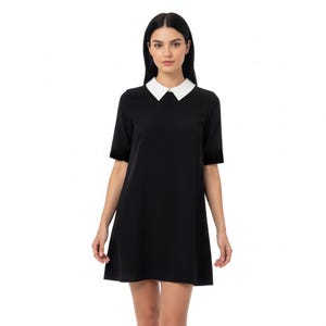 Puede incluir: Vestido negro con cuello blanco. El vestido tiene mangas cortas y una silueta sencilla en forma de A. La modelo lleva el vestido, que llega por encima de las rodillas.