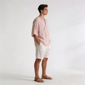 May include: A light pink linen top with a V-neck and short sleeves, paired with white shorts and brown leather sandals. The outfit is casual and relaxed, suitable for warm weather. The sandals have a strappy design.