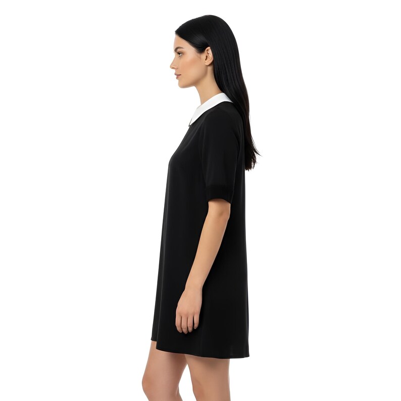 Puede incluir: Un vestido negro con cuello blanco. El vestido tiene mangas cortas y un dise&ntilde;o sencillo y cl&aacute;sico. La modelo lleva el vestido, visto de perfil sobre un fondo blanco.